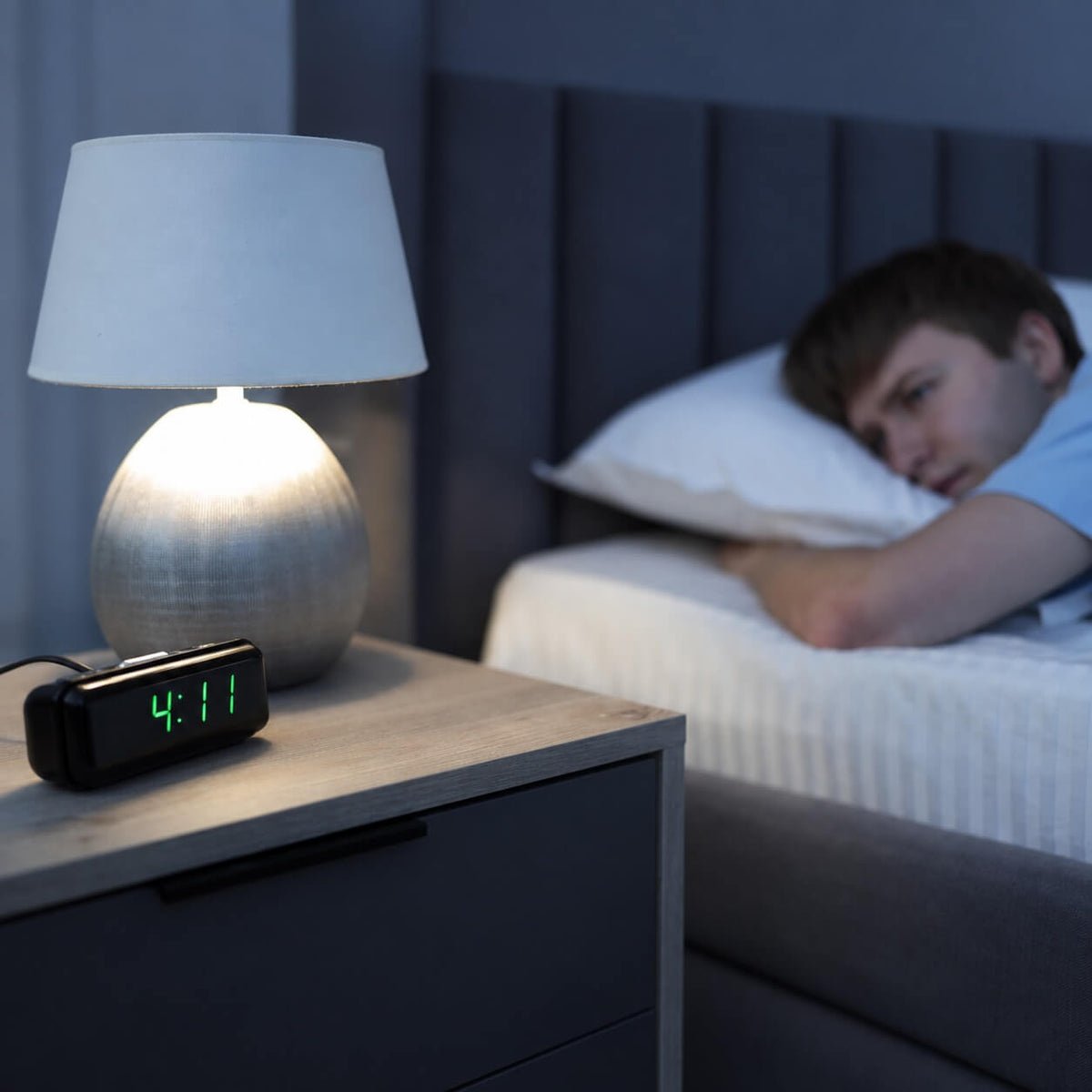 Man who can't sleep, laying in bed staring at his bedside clock