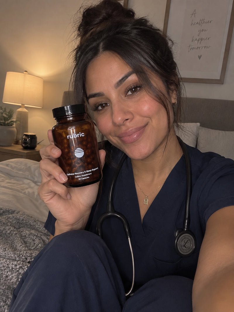 A woman in navy blue medical scrubs holds up a bottle of Rubric dietary supplements in front of a softly lit bedroom background.